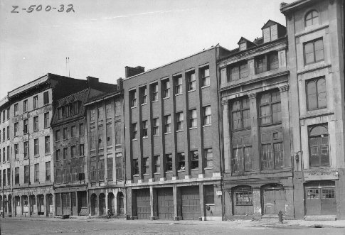 Photographie de commerces et d'édifices de la rue des Commissaires (aujourd'hui rue de la Commune) entre la rue St-Gabriel et la place Jacques-Cartier