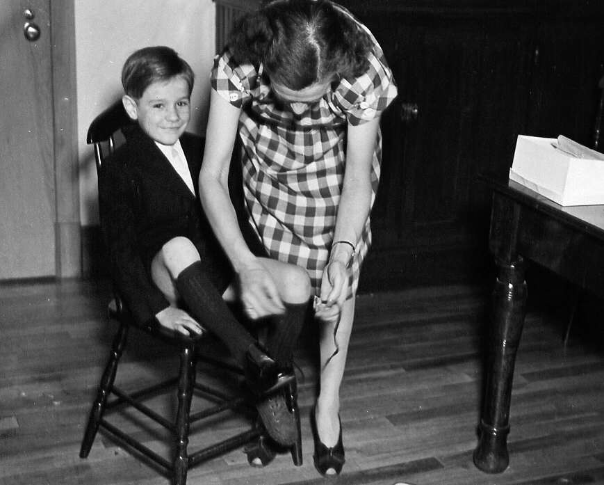 Garçon se faisant attacher ses chaussures par une femme lors d'un reportage sur le placement familiale rue St-Urbain à Montréal en 1947
