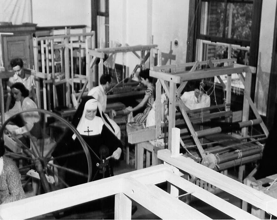 Groupe d'étudiantes travaillant sur des métiers à tisser et une religieuse travaillant au rouet lors d'un cours de tissage à Montréal en 1947