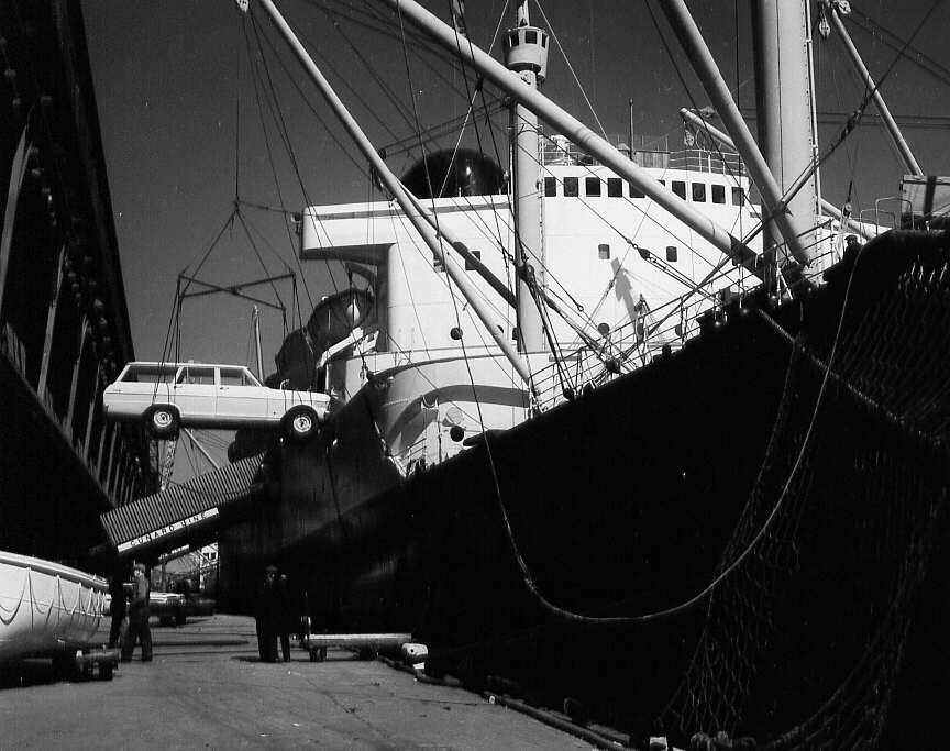 Une grue transportant une voiture près d'un bateau dans le port de Montréal en 1962