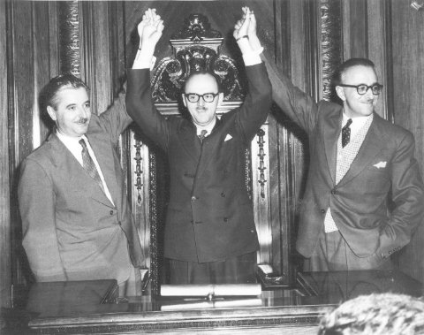 Pierre Desmarais (à gauche) et Pacifique Plante (à droite) levant les bras de Jean Drapeau en signe de victoire au moment de son élection à la mairie de Montréal