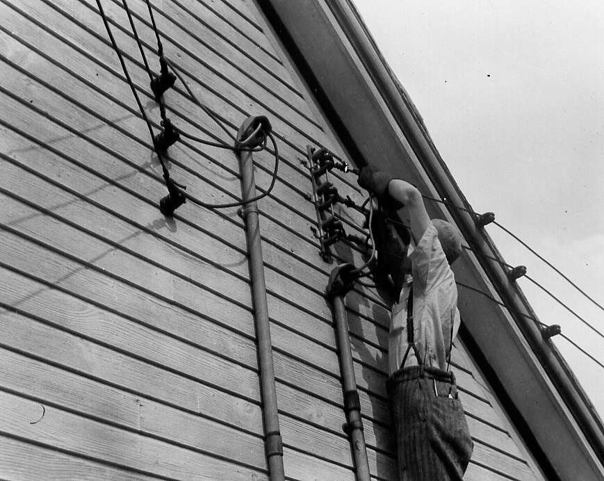 Un homme installe des fils électriques sur une résidence de St-Jean-Baptiste de Rouville en 1947