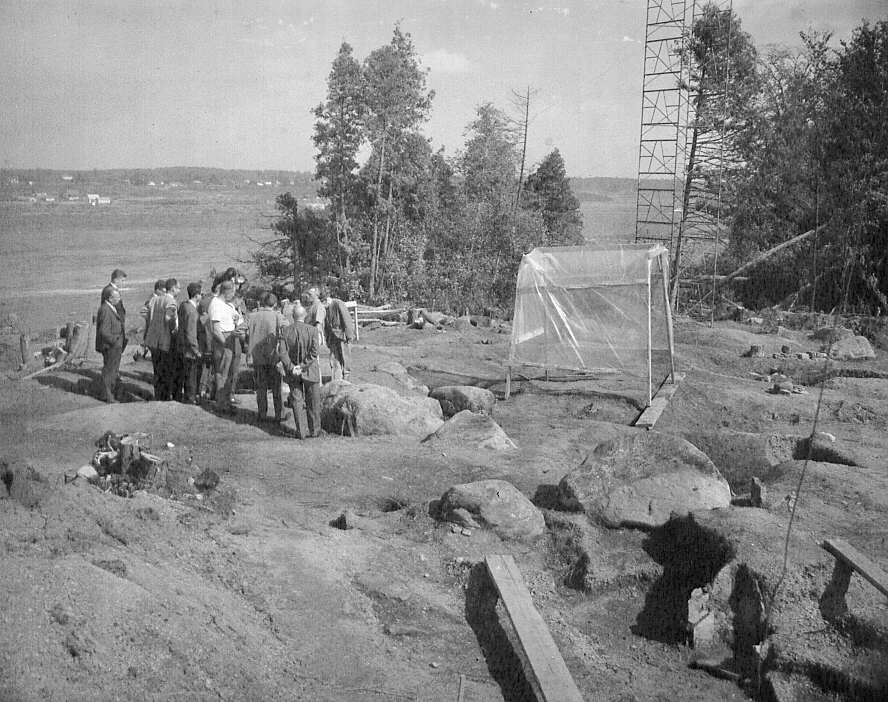 Thomas E Lee, archéologue, et un groupe d'hommes discutant sur le site des fouilles archéologiques pour retracer les vestiges du combat du Long-Sault à Hawksberry en 1961